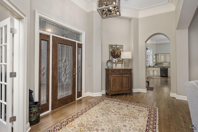 foyer entrance featuring baseboards, arched walkways, dark wood-type flooring, crown molding, and a chandelier