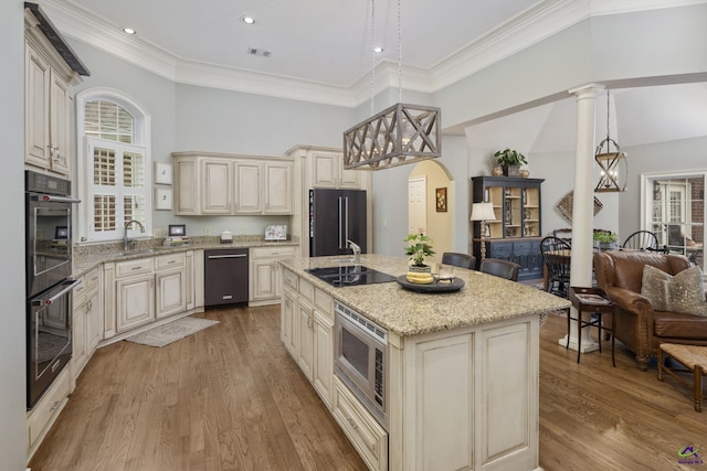 kitchen featuring black appliances, a center island with sink, light stone counters, cream cabinets, and light wood-style floors