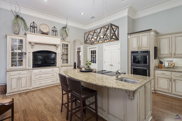 kitchen with light wood finished floors, black appliances, cream cabinets, and a sink