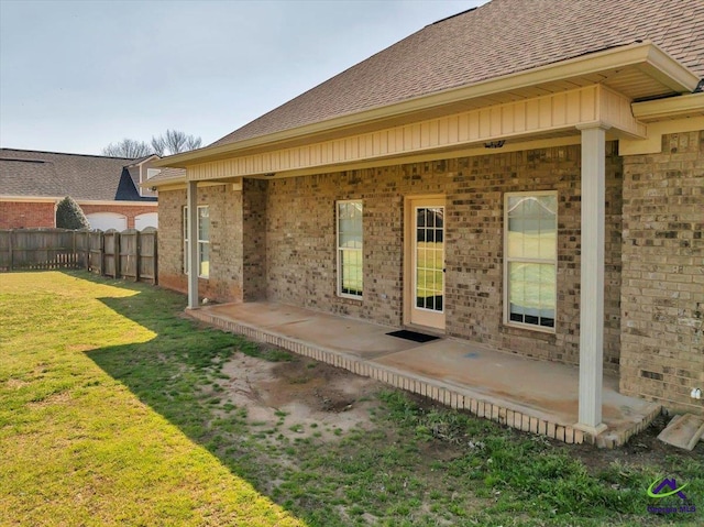 rear view of house with fence, a yard, a shingled roof, a patio area, and brick siding