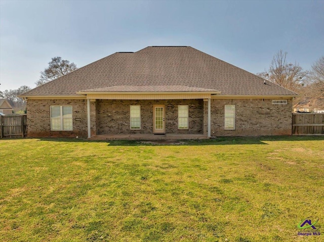 back of house featuring a yard, fence, brick siding, and roof with shingles