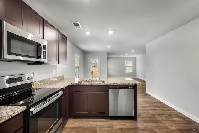 kitchen featuring visible vents, a peninsula, a sink, dark brown cabinetry, and appliances with stainless steel finishes