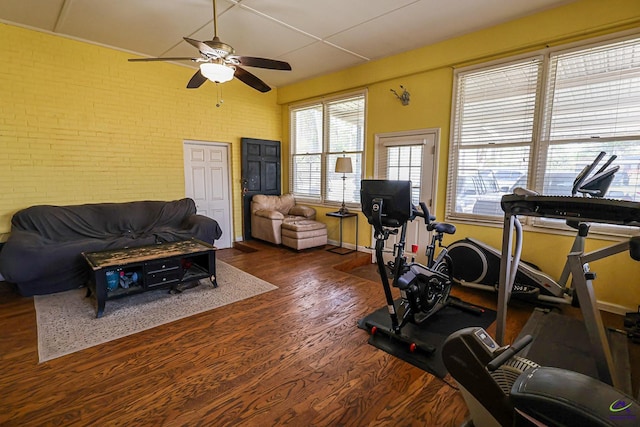 exercise room featuring brick wall, baseboards, ceiling fan, and wood finished floors