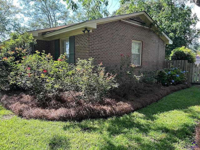 view of side of property with fence, brick siding, and a lawn