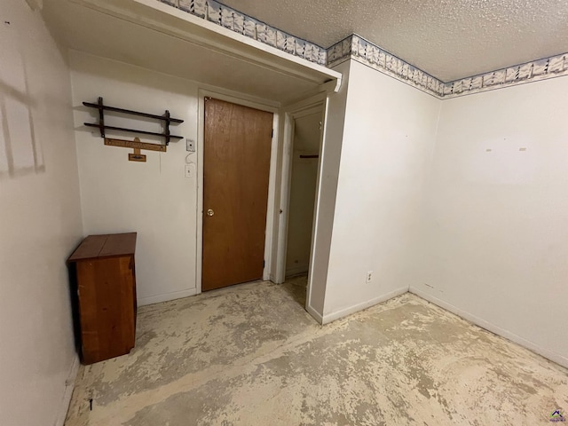 interior space featuring a textured ceiling, concrete floors, and baseboards