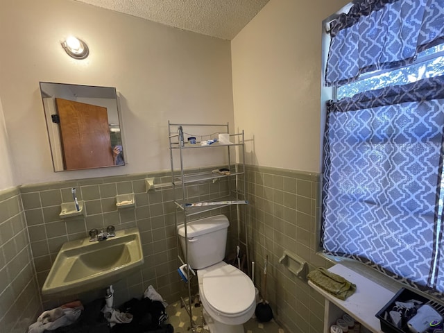 bathroom with tile walls, toilet, wainscoting, a textured ceiling, and a sink