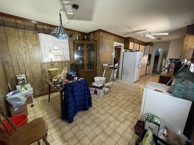 kitchen featuring ornamental molding, freestanding refrigerator, wooden walls, light floors, and ceiling fan