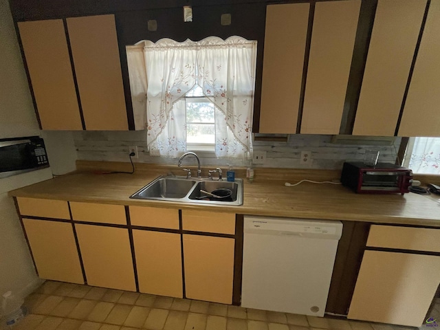 kitchen with a sink, light countertops, black microwave, and white dishwasher