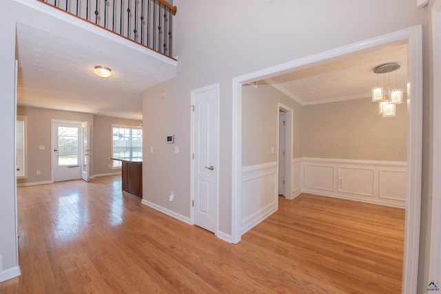 hall with crown molding, wood finished floors, and a wainscoted wall