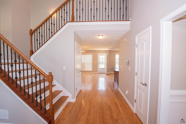 foyer featuring baseboards, visible vents, light wood-style flooring, stairs, and a towering ceiling