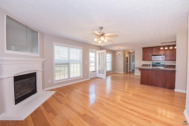 unfurnished living room featuring baseboards, light wood-type flooring, ceiling fan with notable chandelier, french doors, and a glass covered fireplace