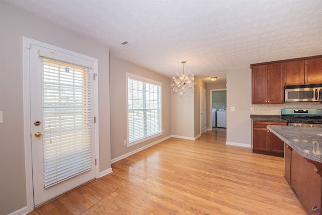 kitchen with baseboards, washing machine and clothes dryer, stainless steel appliances, light wood-style floors, and a notable chandelier