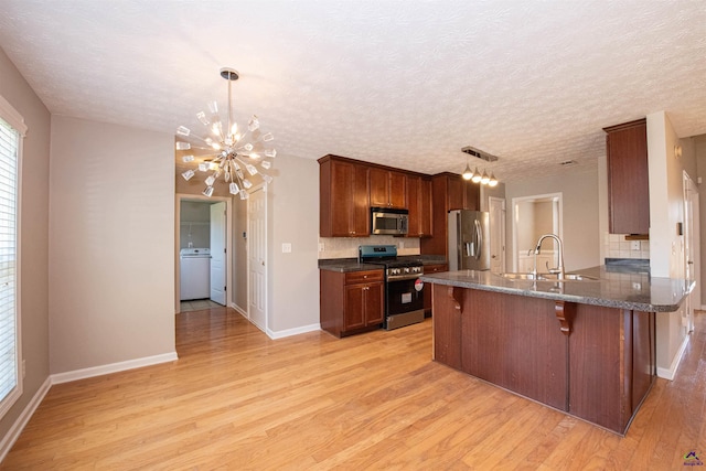 kitchen with a breakfast bar, light wood-type flooring, appliances with stainless steel finishes, washer / clothes dryer, and a sink