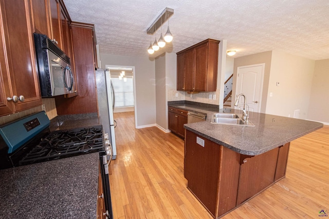 kitchen with a sink, dark countertops, light wood-style floors, appliances with stainless steel finishes, and a peninsula