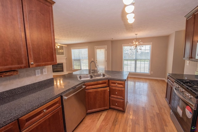 kitchen featuring a sink, light wood-style floors, appliances with stainless steel finishes, a glass covered fireplace, and tasteful backsplash