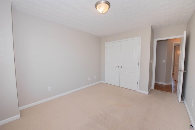 unfurnished bedroom featuring a closet, baseboards, a textured ceiling, and light carpet