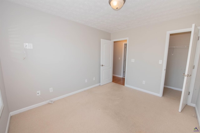 unfurnished bedroom with a textured ceiling, baseboards, a closet, light carpet, and a walk in closet