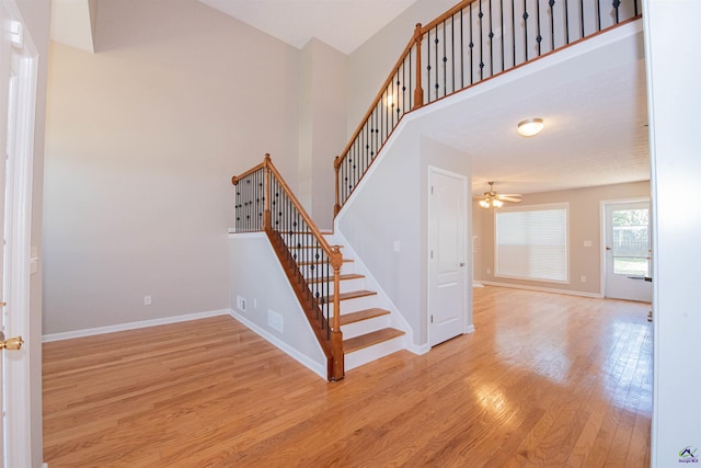 stairway featuring ceiling fan, baseboards, a high ceiling, and wood finished floors