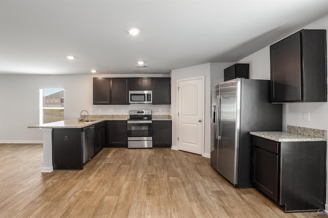 kitchen with a peninsula, recessed lighting, a sink, appliances with stainless steel finishes, and light wood-type flooring