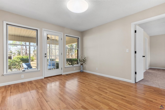 unfurnished room with baseboards, a textured ceiling, and light wood finished floors