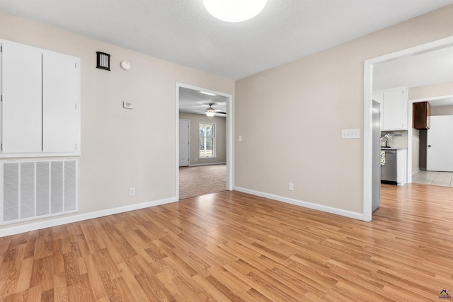 spare room featuring visible vents, baseboards, ceiling fan, light wood-style flooring, and a textured ceiling