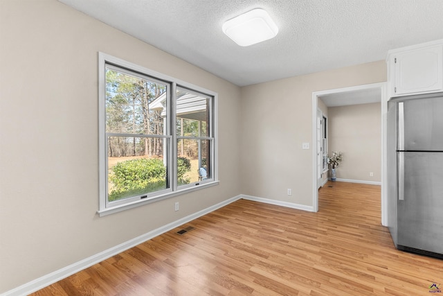 unfurnished dining area featuring visible vents, a textured ceiling, light wood-type flooring, and baseboards