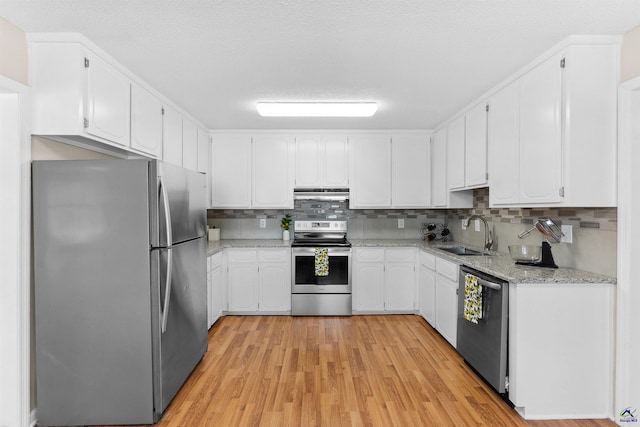 kitchen featuring a sink, stainless steel appliances, white cabinets, light wood-style floors, and under cabinet range hood