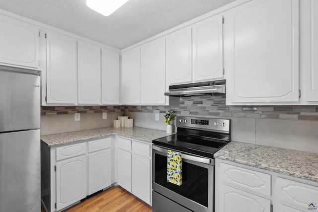 kitchen with under cabinet range hood, white cabinets, stainless steel appliances, and tasteful backsplash