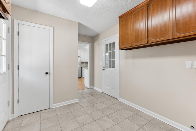 interior space with light tile patterned floors, brown cabinetry, baseboards, and freestanding refrigerator