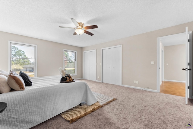 bedroom featuring baseboards, multiple closets, carpet flooring, a textured ceiling, and a ceiling fan