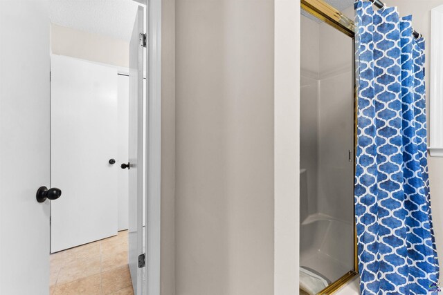 full bath with a textured ceiling, a shower stall, and tile patterned flooring