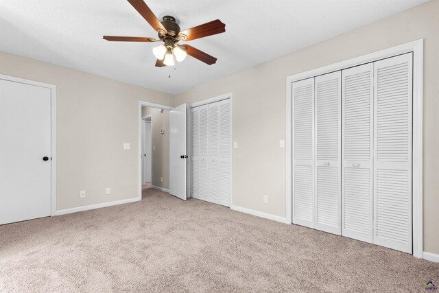 unfurnished bedroom with baseboards, two closets, carpet, and a ceiling fan