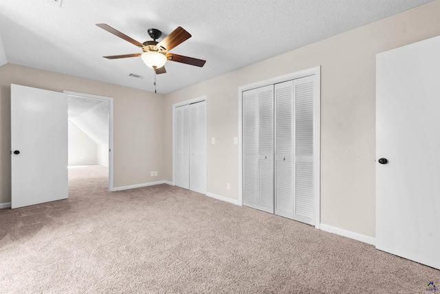 unfurnished bedroom with carpet, baseboards, visible vents, a textured ceiling, and two closets