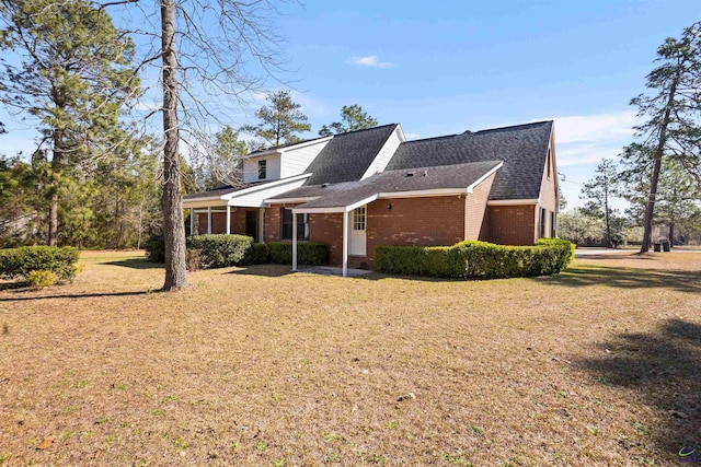 exterior space with brick siding, roof with shingles, and a front lawn