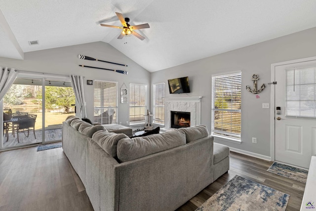 living area with a tiled fireplace, a healthy amount of sunlight, lofted ceiling, and a ceiling fan