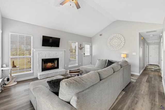 living area featuring a stone fireplace, lofted ceiling, dark wood-style floors, and visible vents