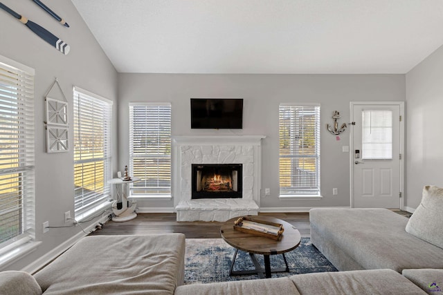 living room featuring a stone fireplace, baseboards, lofted ceiling, and wood finished floors