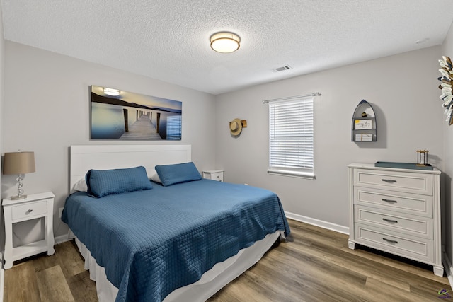 bedroom featuring visible vents, baseboards, a textured ceiling, and wood finished floors