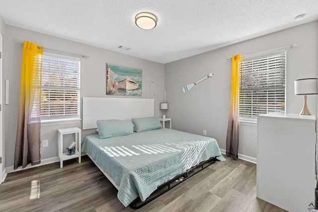 bedroom with visible vents, baseboards, a textured ceiling, and wood finished floors