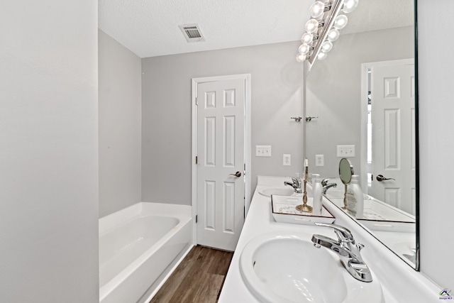 full bathroom featuring visible vents, a textured ceiling, a garden tub, and a sink