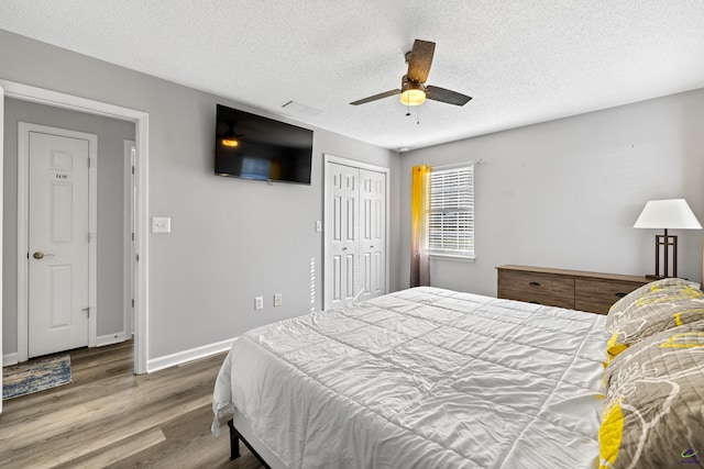 bedroom with a textured ceiling, wood finished floors, a closet, baseboards, and ceiling fan