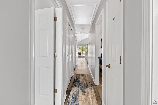 hall featuring visible vents, attic access, and wood finished floors