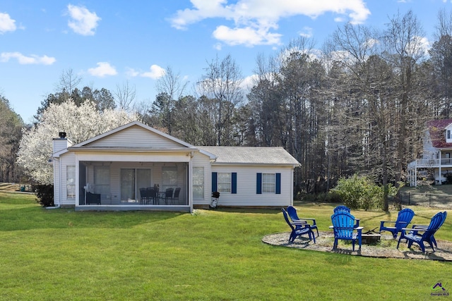 rear view of house featuring a chimney, a lawn, an outdoor fire pit, and a sunroom