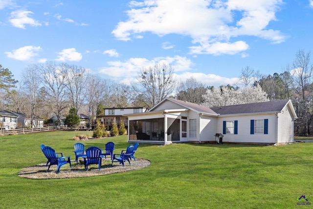 back of property featuring fence, a fire pit, a lawn, and a sunroom