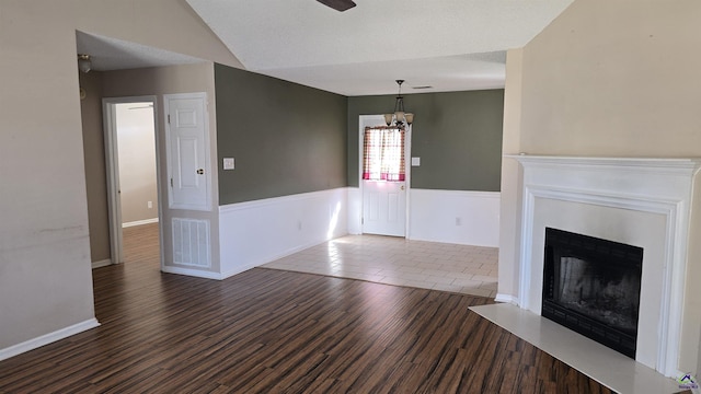 unfurnished living room with visible vents, wood finished floors, wainscoting, a fireplace, and lofted ceiling