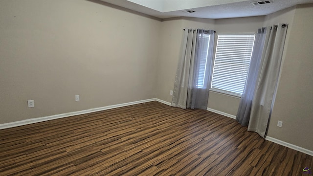 empty room featuring visible vents, dark wood-style floors, baseboards, and a textured ceiling