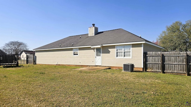 back of house featuring central air condition unit, a lawn, fence, and a chimney