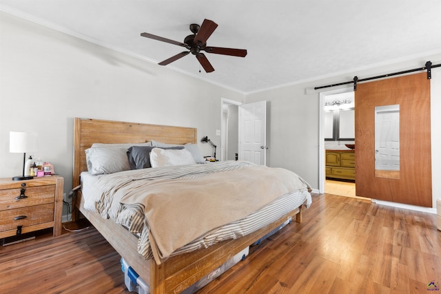 bedroom featuring ceiling fan, a barn door, wood finished floors, and ornamental molding