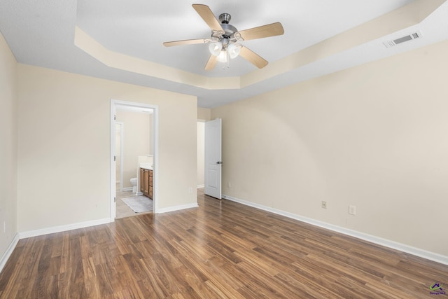 unfurnished bedroom featuring visible vents, connected bathroom, baseboards, wood finished floors, and a raised ceiling