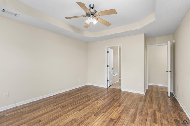 unfurnished bedroom with a tray ceiling, baseboards, visible vents, and wood finished floors